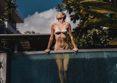 A woman in a bikini relaxes in an infinity pool under the sun surrounded by lush greenery.