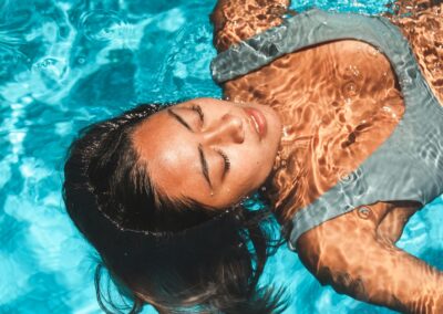 A serene portrait of an Asian woman floating with eyes closed in a vibrant blue pool, exuding relaxation and tranquility.