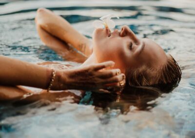 Woman with eyes closed floating peacefully in a Bali swimming pool with a flower