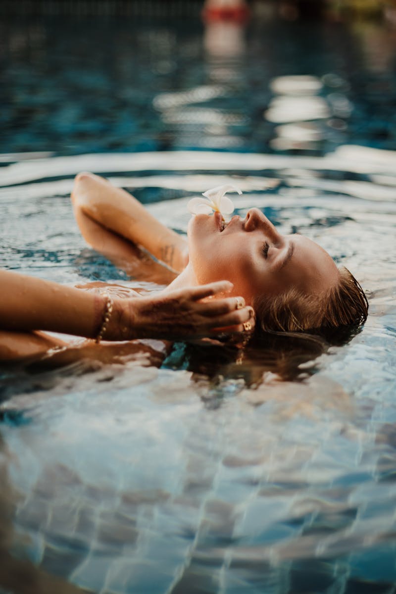 Woman with eyes closed floating peacefully in a Bali swimming pool with a flower